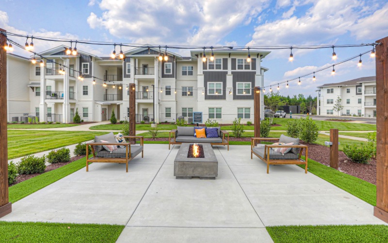 Outdoor fire pit with couches and lights hanging above
